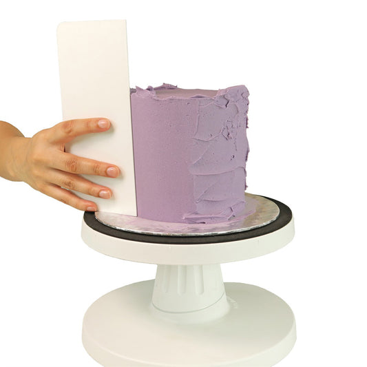 Hand using PME scraper to smooth buttercream on a pink cake for a sharp, professional finish