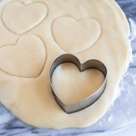 Heart cookie cutter creating heart-shaped impressions in dough on a marble surface.