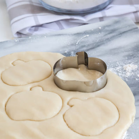 Pumpkin cookie cutter cutting into dough on a marble surface, surrounded by pumpkin-shaped dough cutouts.