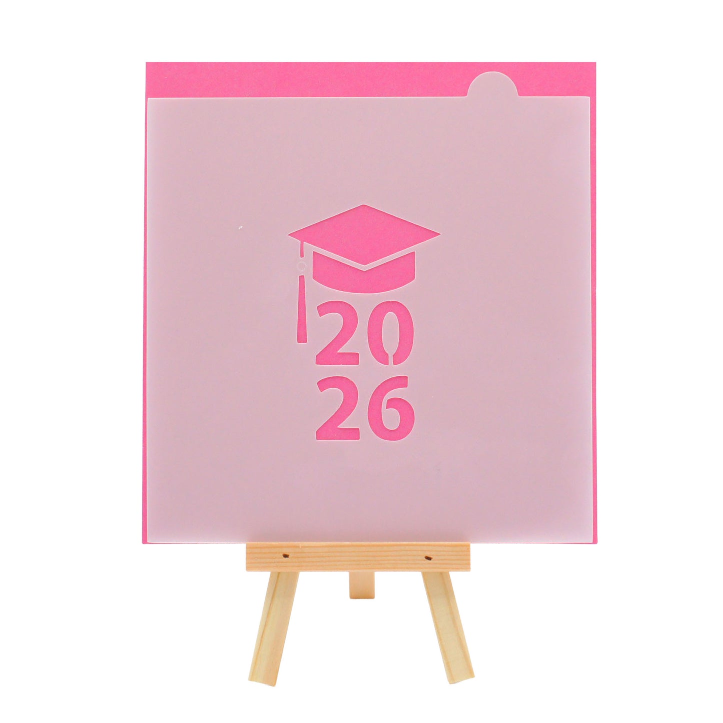 Graduation cap cookie stencil with the year 2026, shown on a bright pink background and displayed on a small wooden easel.