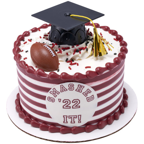 Striped red and white cake topped with a graduation cap, gold tassel, and a 3D football ring.