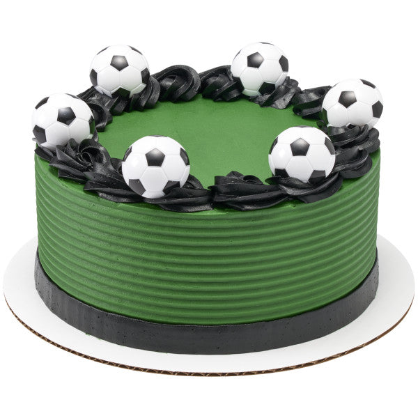 Round green soccer-themed cake decorated with multiple black and white 3D soccer ball rings and black frosting swirls.