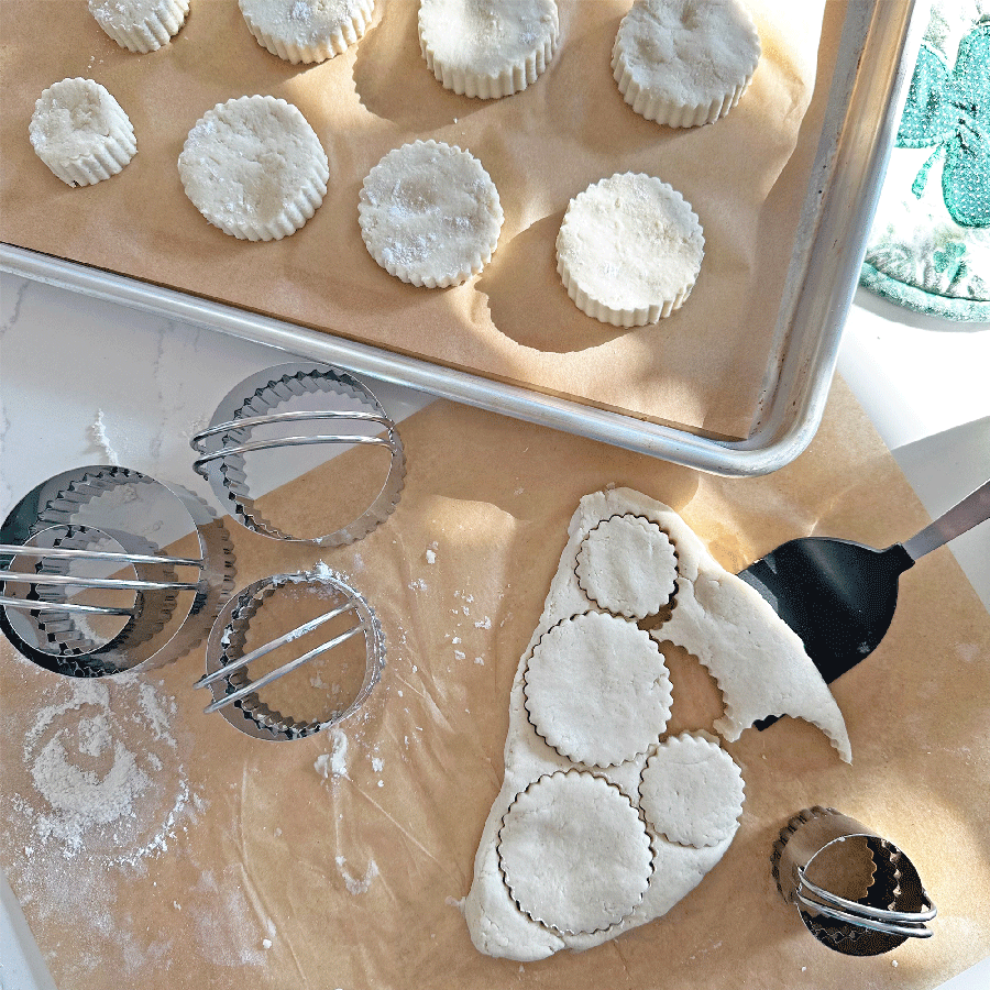Fluted biscuit cutters in use, cutting dough on parchment paper with baked biscuits in the background.