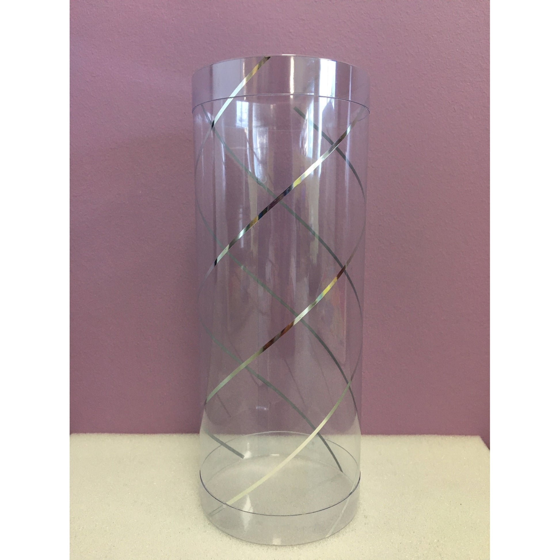 The image displays a clear acetate plastic cylinder, featuring a simple yet elegant design with crisscrossing metallic lines that spiral around the exterior. The transparent nature of the cylinder allows for the contents to be visible, making it ideal for presenting and showcasing items within.