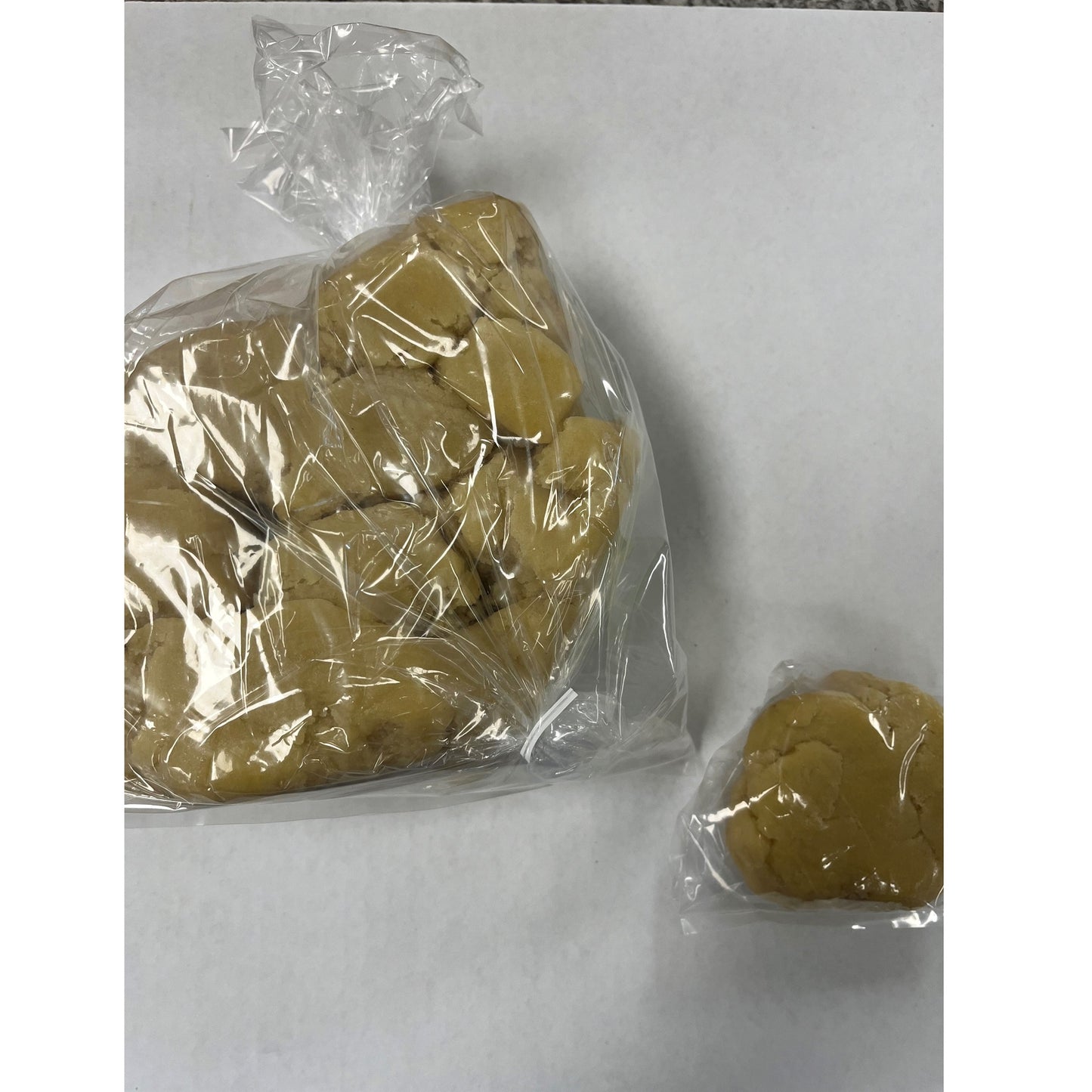 Plastic-wrapped portion of almond paste on a white background, with a larger bag and a smaller individual portion shown for reference.