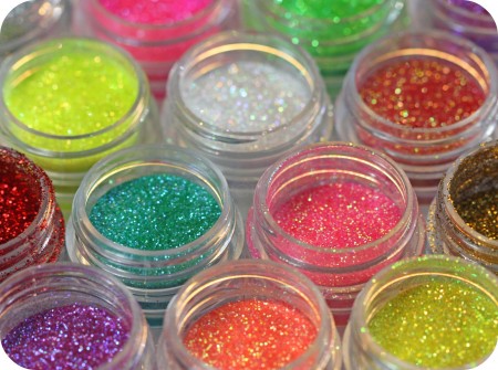 Assorted jars of Galaxy Glitter Dust in various vibrant colors, including green, pink, gold, and turquoise, arranged in a colorful flat lay.
