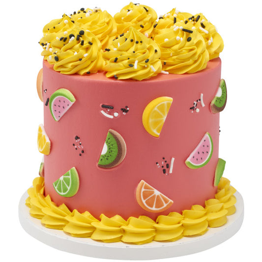 Tall cake with pink frosting and yellow swirls, decorated with assorted fruit slice sugar toppers.