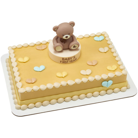 Rectangular first birthday sheet cake decorated with pastel heart accents and piped borders, topped with a brown teddy bear on a round “Baby’s First Year” base from the Beary First Year Cake Kit.