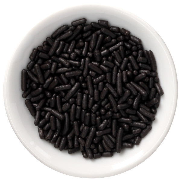 Top-down view of a white bowl filled with black naturally dyed rod-shaped sprinkles on a white background.