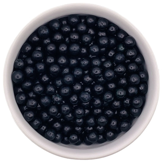Top-down view of a white bowl filled with 7mm glossy black sugar pearls, used for decorating cakes and desserts.
