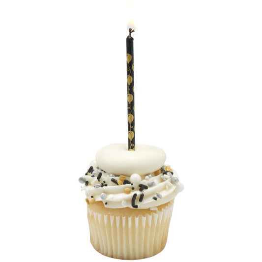 Vanilla cupcake with white frosting, black and gold sprinkles, and a white fondant topper, finished with a lit black candle featuring a gold balloon pattern.
