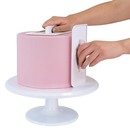 Hands using PME cake smoothers on a tall pink fondant-covered cake to create smooth sides and sharp edges.