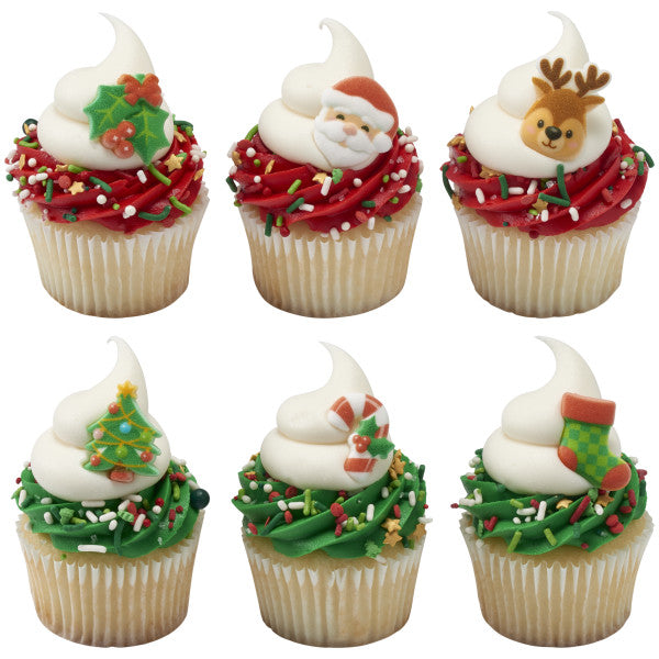 Six vanilla cupcakes with red or green frosting swirls and holiday sprinkles, each topped with a pressed sugar decoration such as holly, Santa face, reindeer head, Christmas tree, candy cane, and stocking.