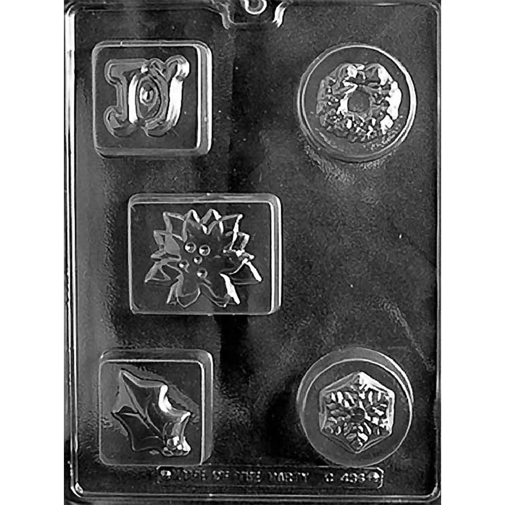 Clear plastic chocolate mold with five assorted Christmas cavities, including a JOY plaque, wreath, poinsettia, holly leaf, and snowflake design, shown on a dark background.