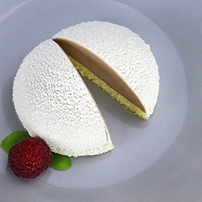 White velvet-sprayed dome dessert with smooth matte finish, sliced open to show layered interior