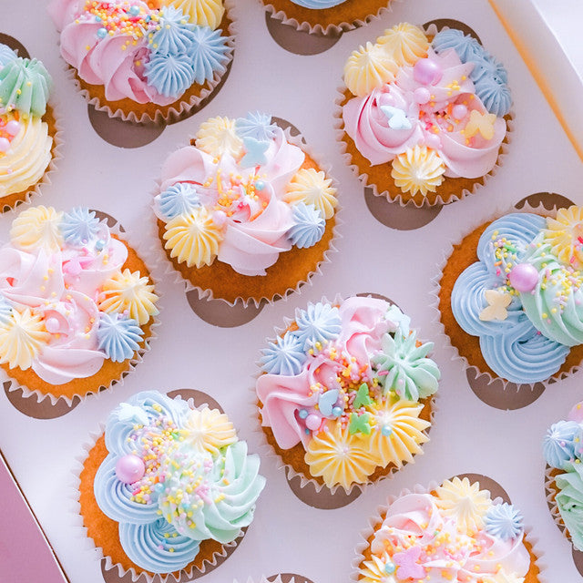 Cupcakes topped with pastel buttercream in Blue Bell, Baby Pink, Lemon, and Sage, decorated with sprinkles and piped florals