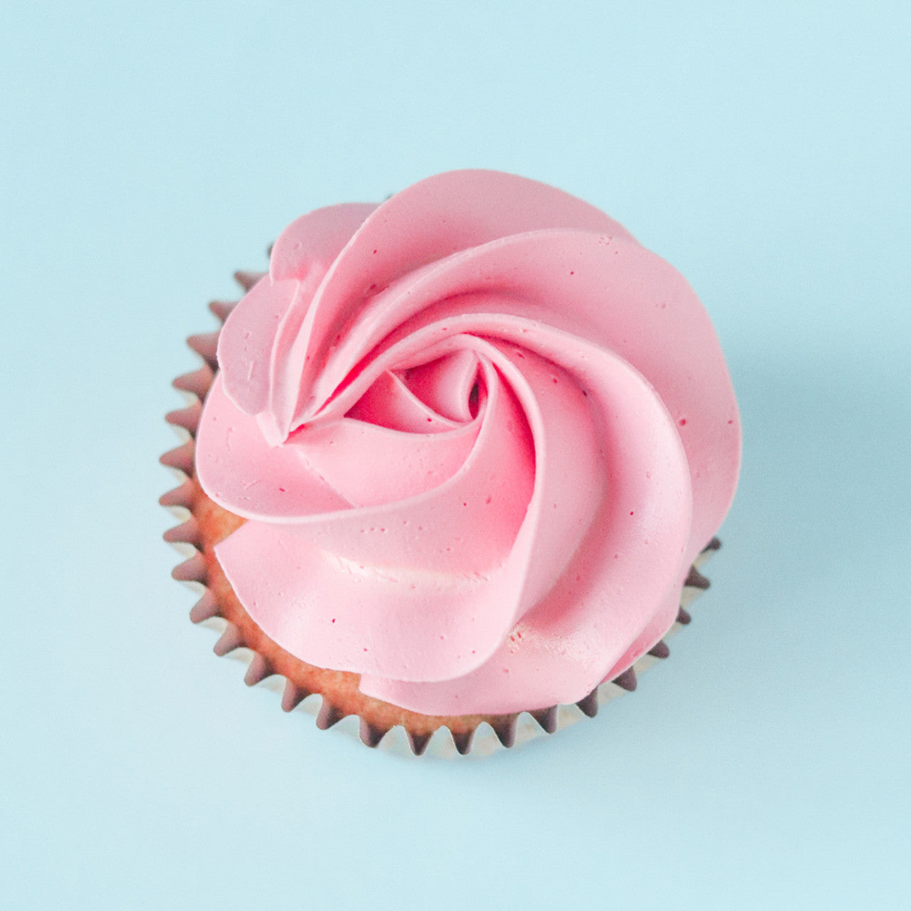 Cupcake topped with a swirl of bright pink buttercream colored with Colour Mill Candy, on a light blue background
