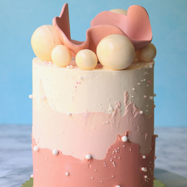 Elegant pink ombré cake with Dusk-toned buttercream, white pearls, and sculpted chocolate decoration.
