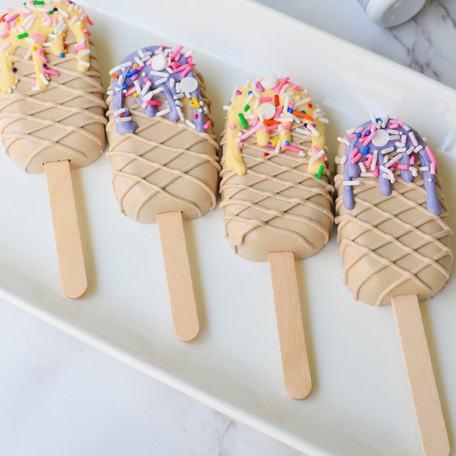 Dessert popsicles coated in Latte-colored chocolate, decorated with colorful drizzle and sprinkles.