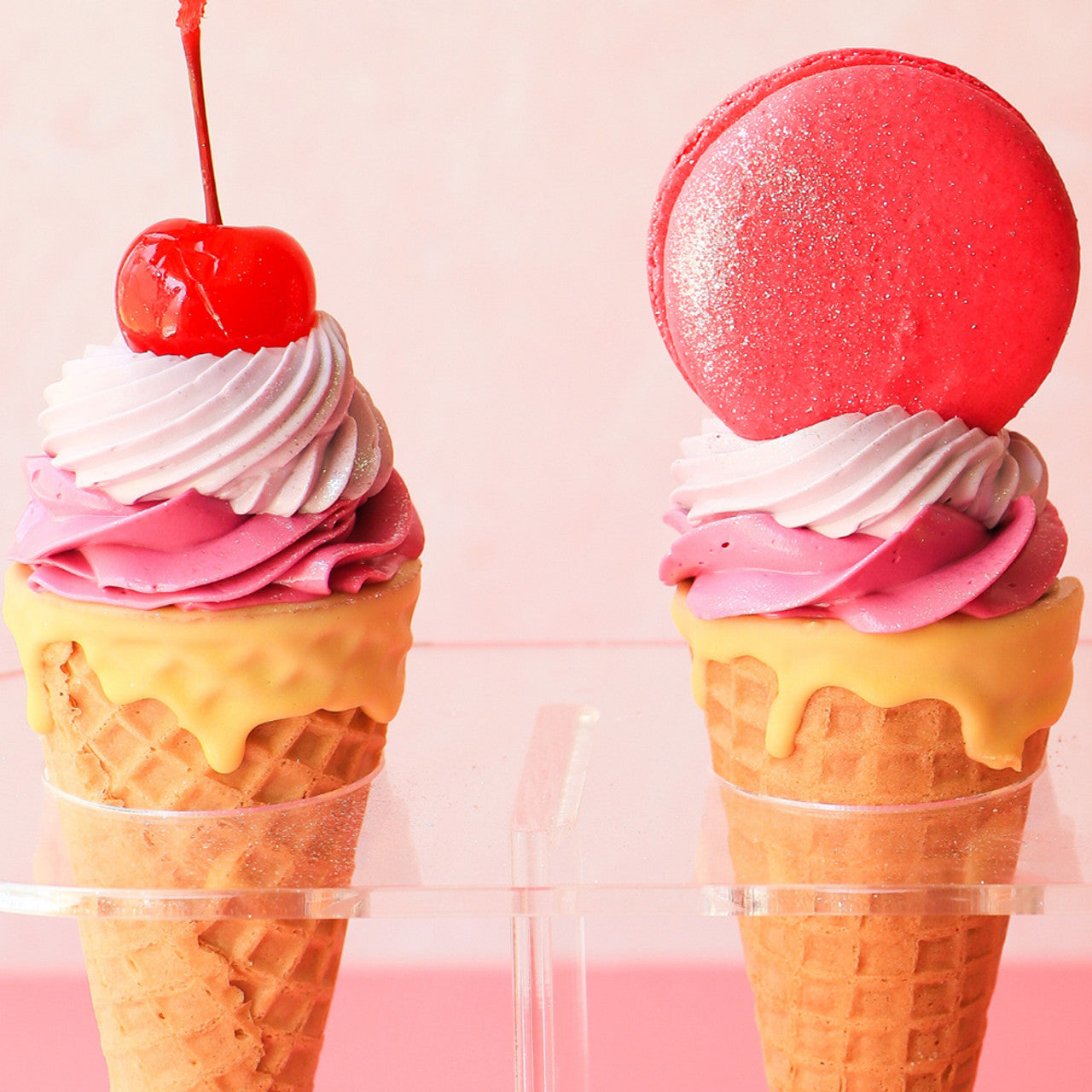 Ice cream cone cupcakes topped with lilac and pink swirled frosting, cherries, and macarons.