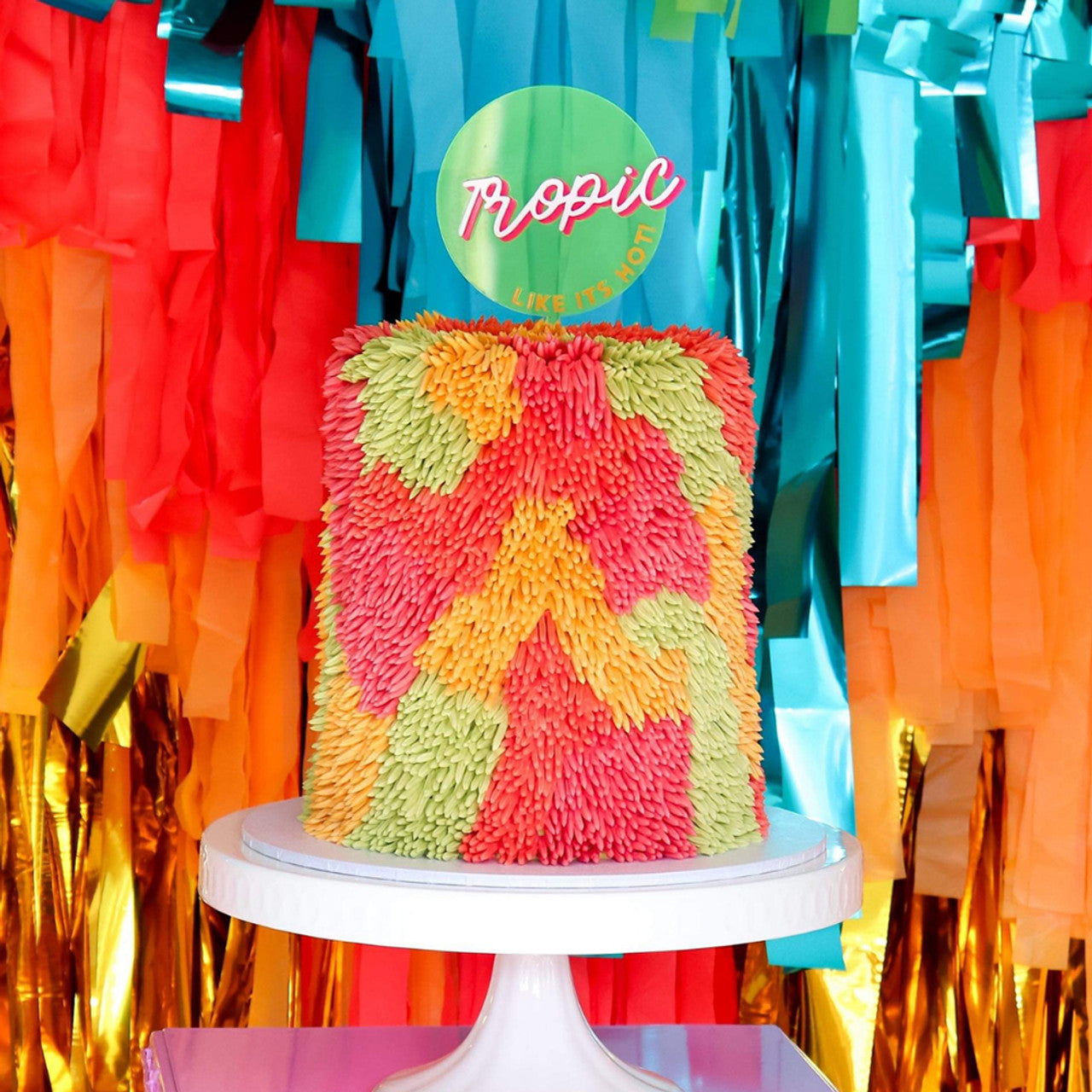 Decorative cake featuring tropical-themed piping in mango, kiwi, and melon shades with bold party backdrop.