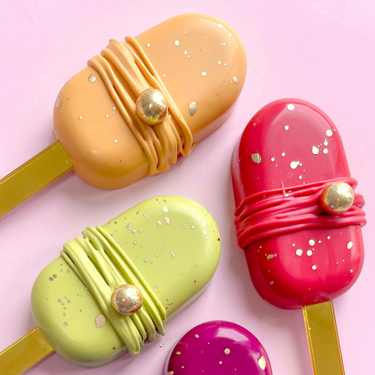 Cakesicles decorated with glossy pink, orange, green, and purple coatings, featuring Melon pink prominently with gold accents.