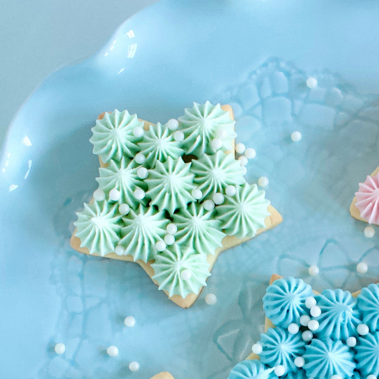 Iced star-shaped sugar cookie topped with pastel mint green buttercream stars and white sugar pearls using Colour Mill Mint