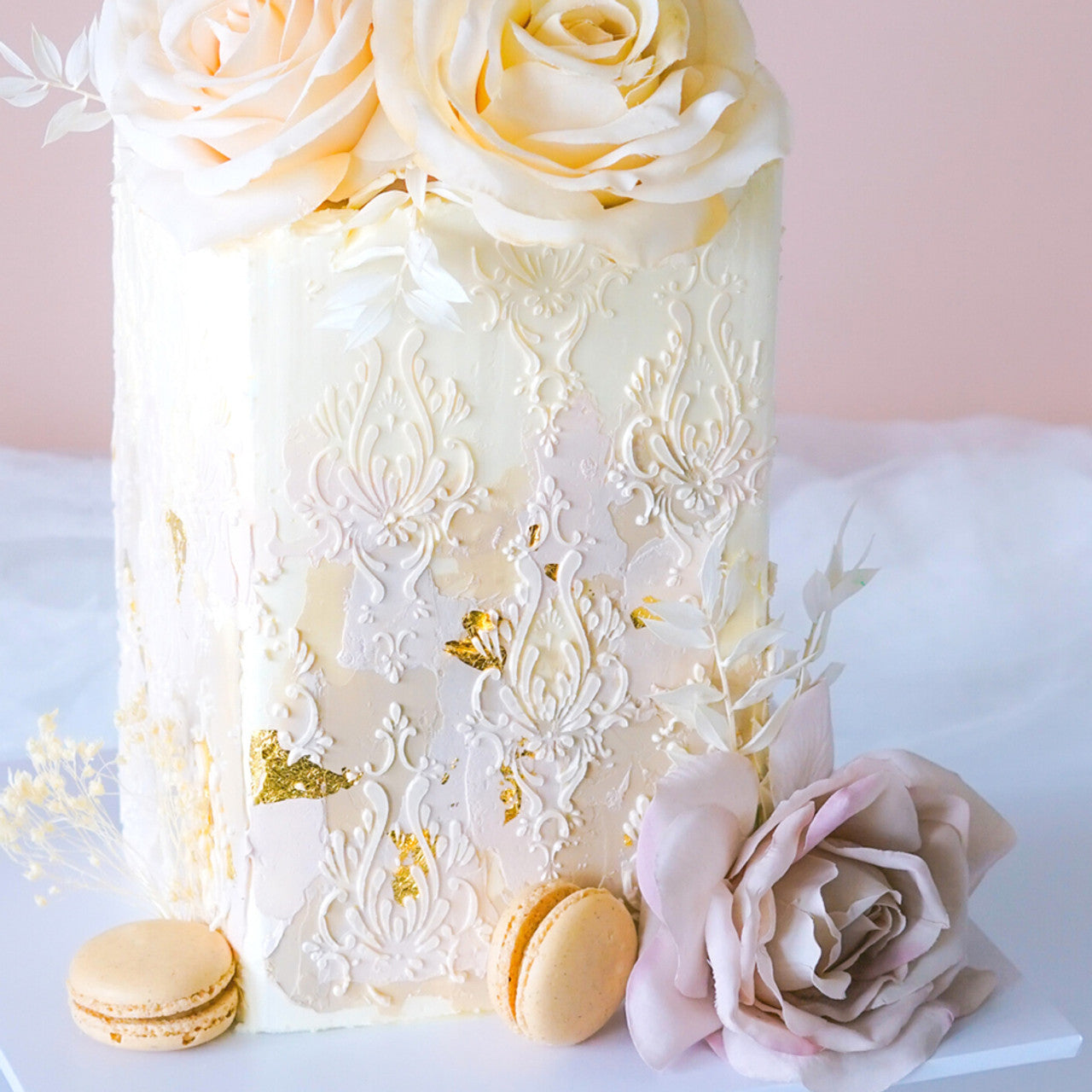 Luxury wedding cake decorated with soft nude buttercream, white floral textures, and gold leaf details using Colour Mill Nude