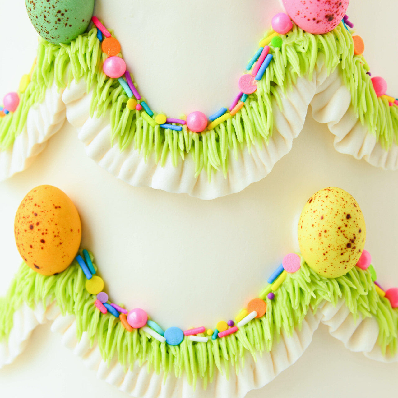 Easter-themed cake decorated with piped grass, pastel sprinkles, and bright fondant eggs over a clean white base