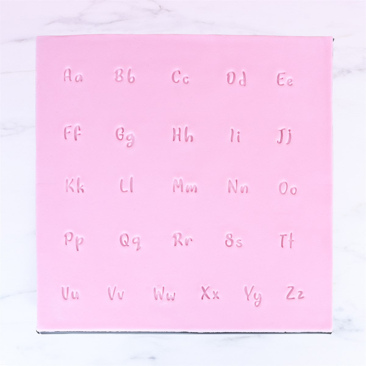 Stamped letter impressions from PME Fun Fonts Collection 3 showing cursive-style alphabet on pink fondant.
