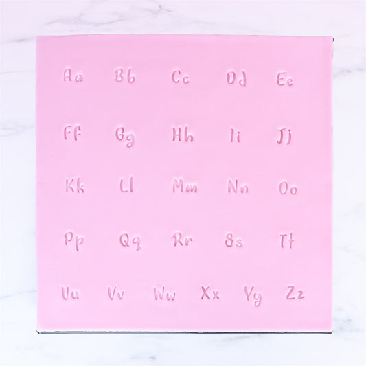 Stamped letter impressions from PME Fun Fonts Collection 3 showing cursive-style alphabet on pink fondant.