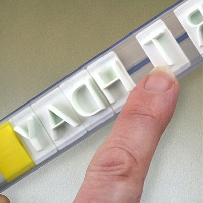 Close-up of fingers assembling letters in PME Create N Press guide rail for neat cake message creation.