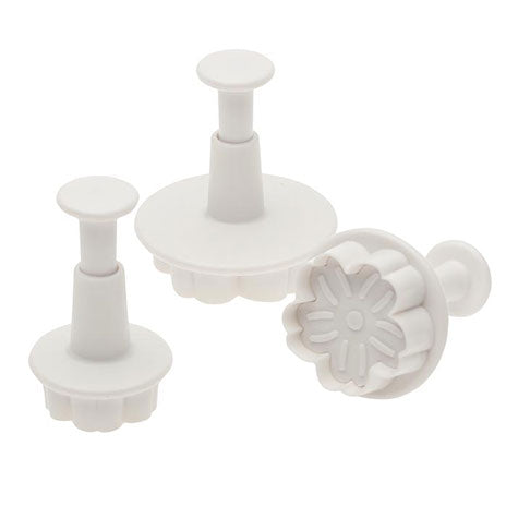 Three-piece daisy plunger cutter set made of white plastic, shown with detailed daisy-shaped cutting ends and spring-action handles for fondant or gum paste.