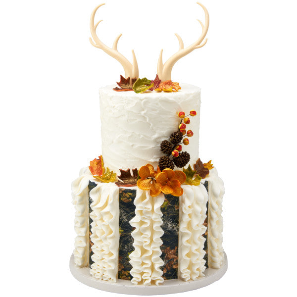 Tall fall-themed cake with ruffle accents and autumn leaves, topped with deer antlers for a woodland vibe.