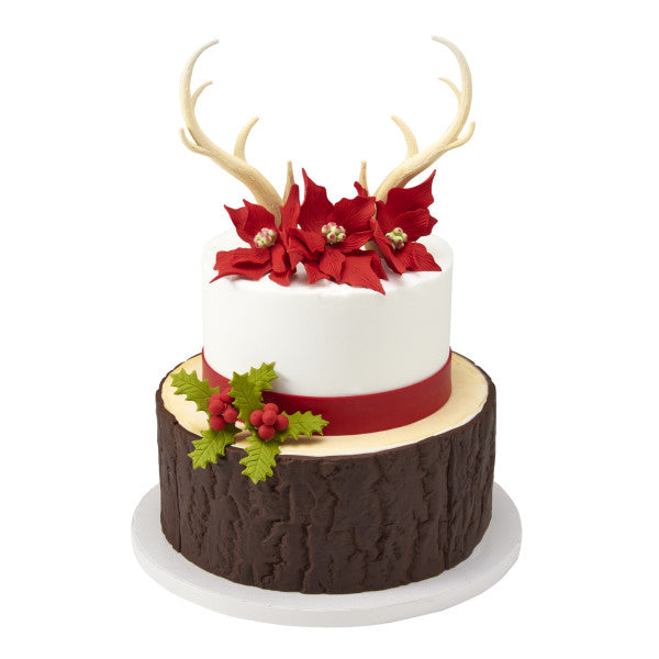 Two-tier Christmas cake with poinsettias and deer antler toppers, styled with a tree bark-inspired bottom tier.