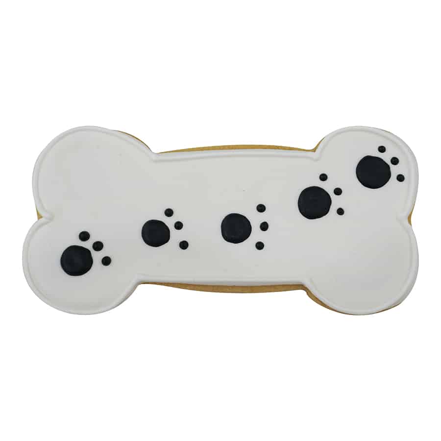 Dog bone-shaped sugar cookie decorated with smooth white icing and black paw print details.