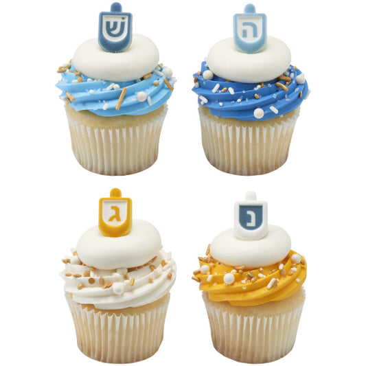 Four vanilla cupcakes with swirled frosting in blue, white, and golden yellow, topped with pressed sugar dreidel decorations and sprinkled with white and gold sprinkles.