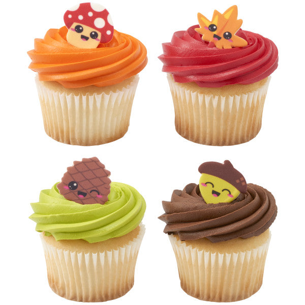 Four cupcakes topped with colorful frosting and decorated with smiling pressed sugar figures, including a mushroom, leaf, pine cone, and acorn.