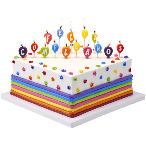 Square rainbow-striped birthday cake topped with lit Feliz Cumpleaños balloon candles and multicolored star decorations