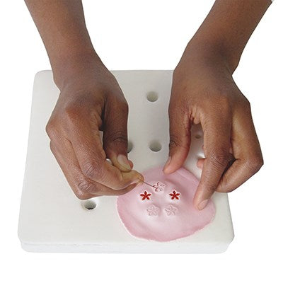 Hands using the JEM Roller Pad to cut floral shapes from pink fondant using a cutter and pin tool.