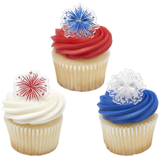 Three vanilla cupcakes topped with white, red, and blue frosting swirls, each decorated with a foil fireworks cupcake ring in red, blue, or silver.