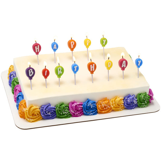 Rectangular birthday cake topped with rainbow balloon candles spelling "HAPPY BIRTHDAY" and finished with colorful piped rosettes