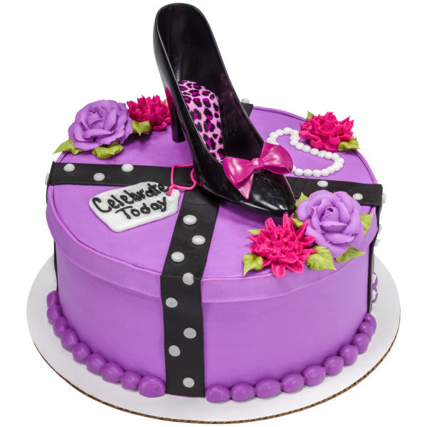 Round purple cake with black high heel topper, floral accents, and fondant decorations including a “Celebrate Today” tag.