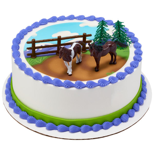 Round cake with horses cake topper set on an icing pasture with blue sky and fence.