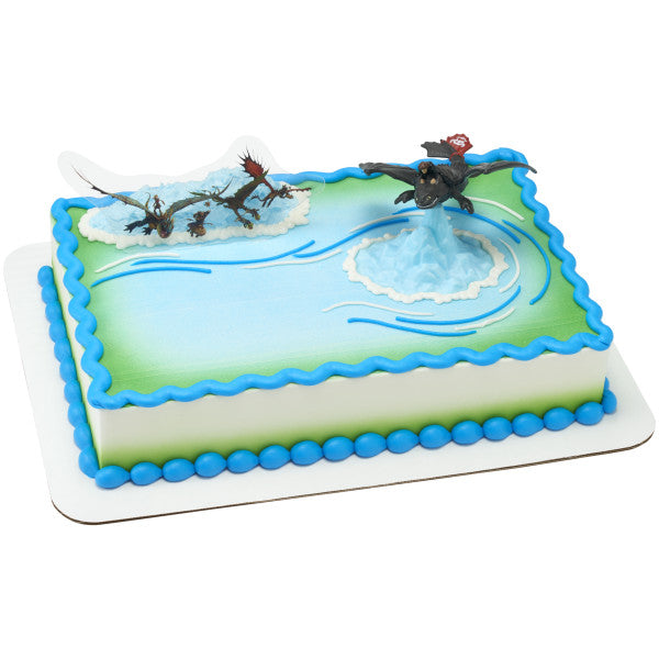 Rectangular cake with green and blue icing, topped with Toothless pivoting figurine and dragon background pick.