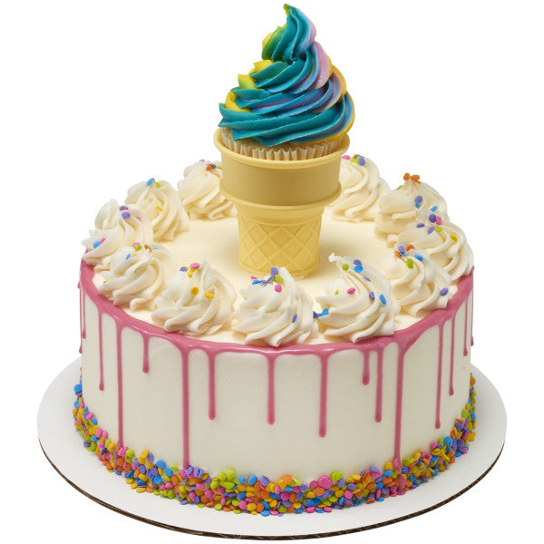 Round white cake with pink drip icing and rainbow sprinkle border, topped with white frosting swirls and a cupcake set inside an assembled yellow ice cream cone topper.
