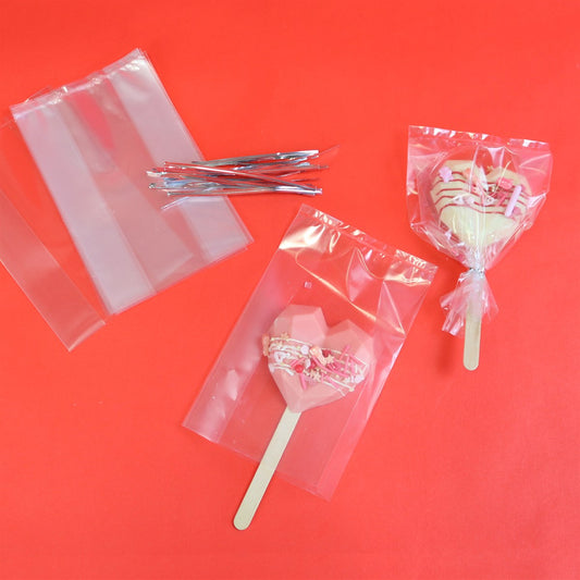 Clear PME lollipop bags displayed with heart-shaped chocolate pops and included silver twist ties on a red background.