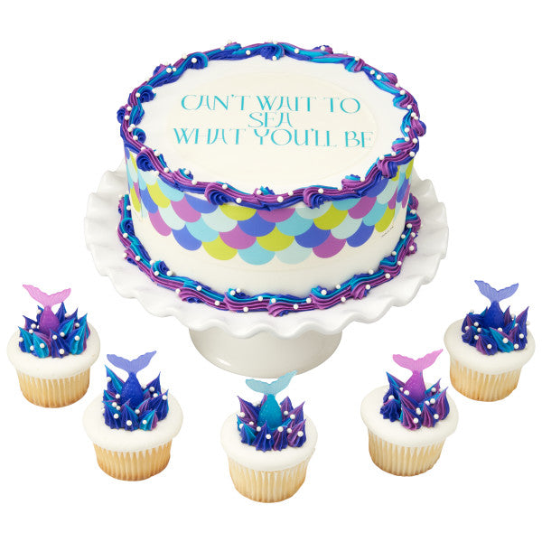Decorated mermaid-themed cake with scale pattern and matching cupcakes, all topped with mermaid tails and sea-themed accents.