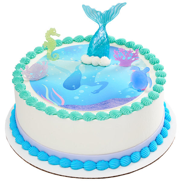 Round cake with sea-themed printed topper and teal frosting border, featuring Mystical Mermaid toppers including a mermaid tail, seahorse, turtle, shell crown, and coral.