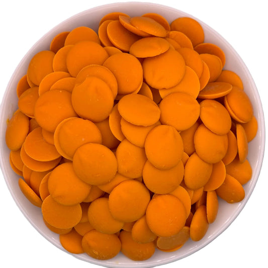Top-down view of a bowl packed with bright orange candy melts, flat round discs used for melting in baking and confectionery.